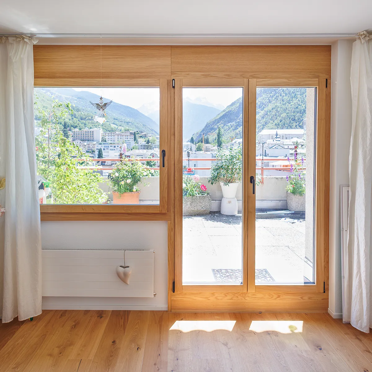 Innenansicht mit Holzfenster und Balkontür, Blick auf Berge und Balkon mit Pflanzen.