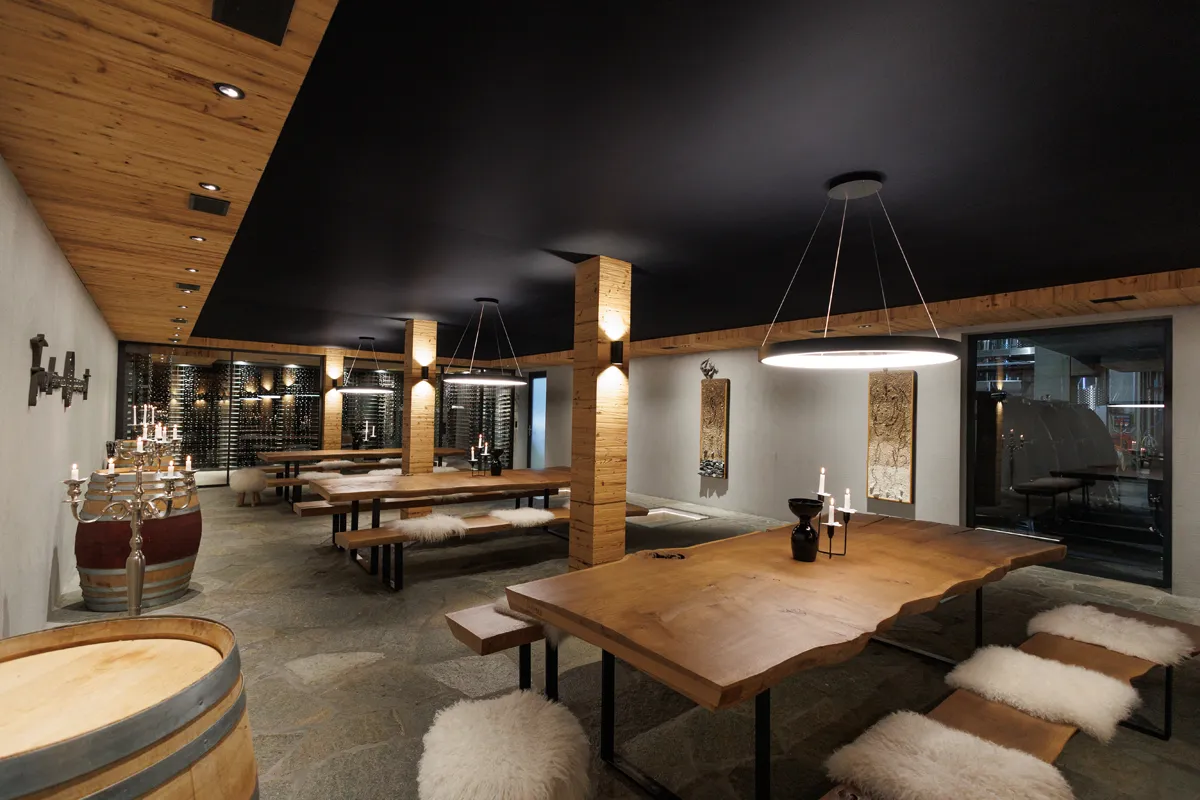 Gemütliches Restaurant mit Holztischen, schwarzen Decke und warmem Licht.